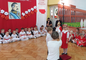 Dziewczynka ubrana na biało - czerwono oraz chłopiec ubrany na galowo recytują wiersz.